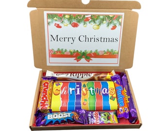 May include: A brown cardboard box with a Christmas-themed lid that says "Merry Christmas". The box is open and filled with various chocolate bars, including Galaxy Ripple, Crunch, Christmas, Boost, Freddo, and Cadbury Fudge.