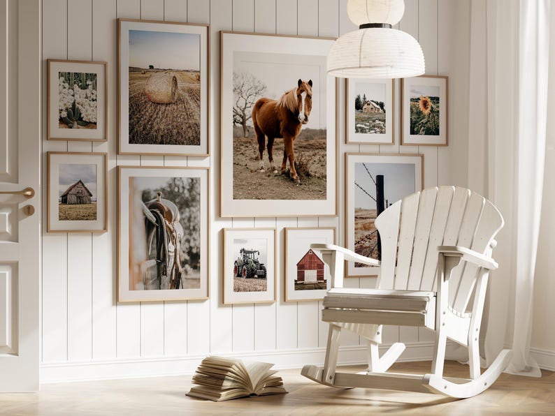 May include: A white rocking chair with a wooden frame sits in front of a wall with framed pictures of horses, barns, and farm scenes. The pictures are in various sizes and are arranged in a grid pattern.
