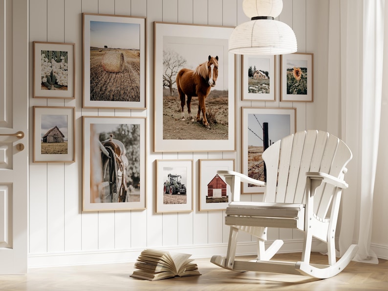 May include: A white rocking chair with a wooden frame sits in front of a wall with framed pictures of horses, barns, and farm scenes. The pictures are of various sizes and are arranged in a grid pattern.