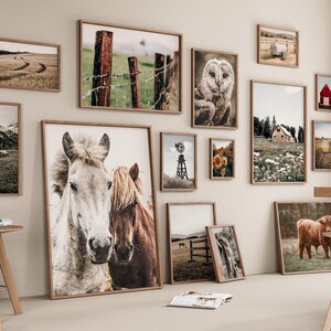 May include: A gallery wall featuring a variety of framed prints with rustic and farmhouse themes. The prints include images of horses, owls, barns, and landscapes. The prints are arranged in a symmetrical pattern on a light beige wall.