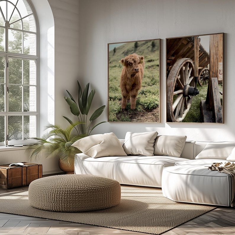 May include: Two framed prints of nature scenes. The left print shows a brown Highland calf standing in a grassy field. The right print shows a wooden wagon wheel with a wooden cart in the background.