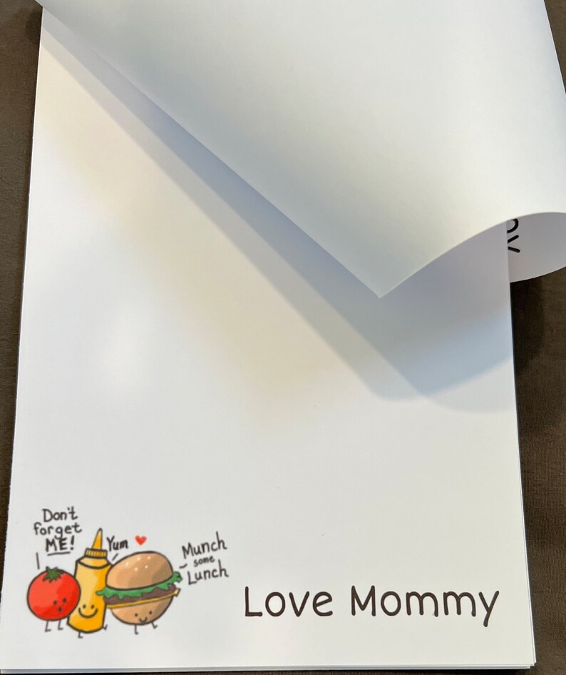May include: White notepad with a cartoon illustration of a tomato, ketchup bottle, and hamburger with the text "Don't forget ME! Yum Munch some Lunch Love Mommy".