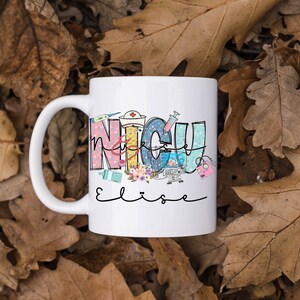 Puede incluir: Taza de cer&aacute;mica blanca con un dise&ntilde;o colorido que dice "NICU Nurse" con un estetoscopio, una jeringa y otros equipos m&eacute;dicos. El nombre "Elise" est&aacute; escrito en cursiva debajo del dise&ntilde;o.