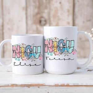 Puede incluir: Dos tazas de cer&aacute;mica blanca con un gr&aacute;fico colorido de la palabra "NICU" con s&iacute;mbolos m&eacute;dicos y los nombres "Elise" y "Felicia" escritos debajo.