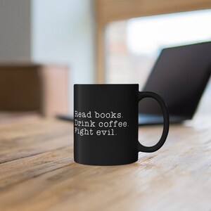 May include: Black coffee mug with white text that reads "Read books. Drink coffee. Fight evil."