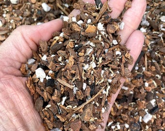May include: A close-up of a handful of brown, black, and white bark chips. The chips are a mix of sizes and shapes, and they are used as a soil amendment or mulch.