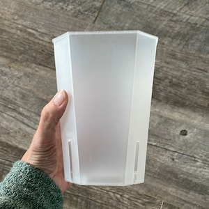 May include: A white plastic hexagonal planter with two drainage holes on the sides.