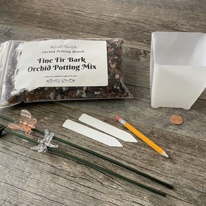 May include: A kit for growing orchids, containing a bag of fine fir bark orchid potting mix, a white plastic pot, two white plant labels, three green plant stakes, a pencil, and two dragonfly-shaped plant clips.