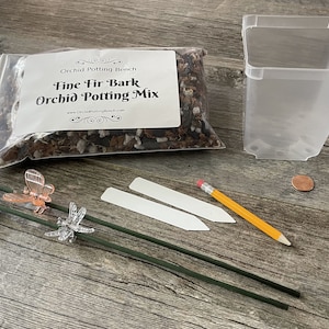 May include: A set of orchid potting supplies including a bag of fine fir bark orchid potting mix, a clear plastic pot, two white plant labels, two green stakes with butterfly and dragonfly accents, and a yellow pencil.
