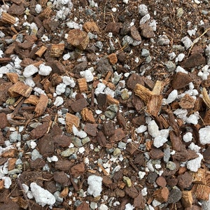 May include: Close-up of a mixture of brown and white materials, likely used as a soil amendment or potting mix. The mixture includes small pieces of coconut husk, white pebbles, and brown soil.