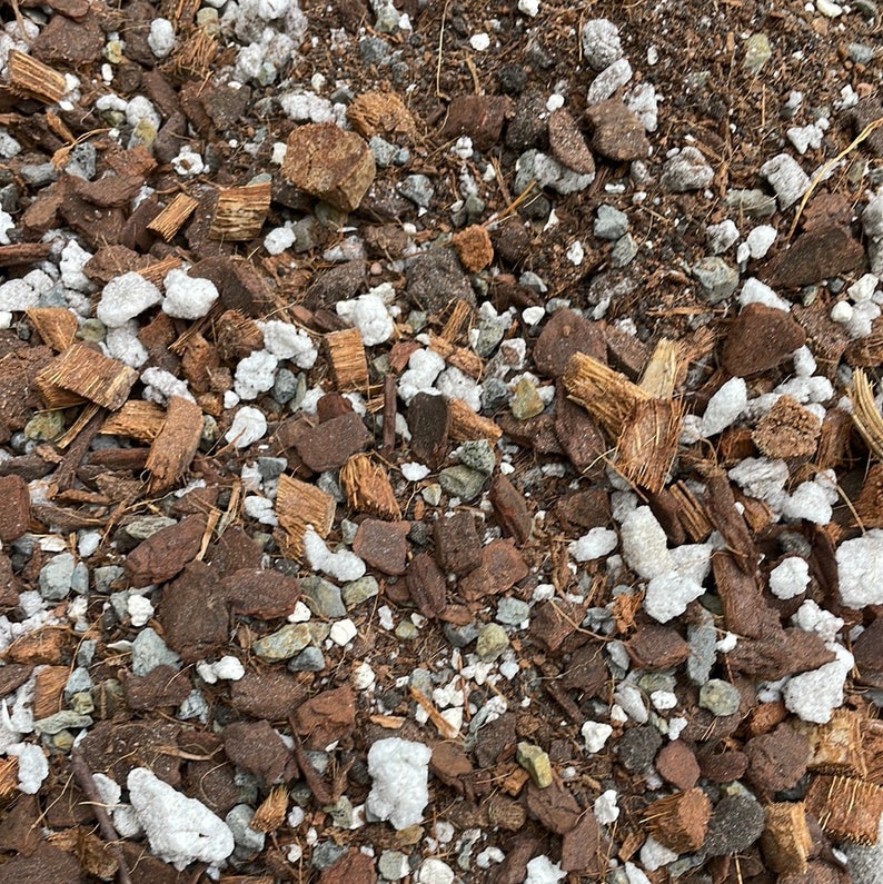 May include: Close-up of a mixture of brown and white materials, likely used as a soil amendment or potting mix. The mixture includes small pieces of coconut husk, white pebbles, and brown soil.