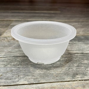 May include: A frosted white plastic plant pot with a round shape and a slightly flared rim. The pot has four small feet on the bottom.