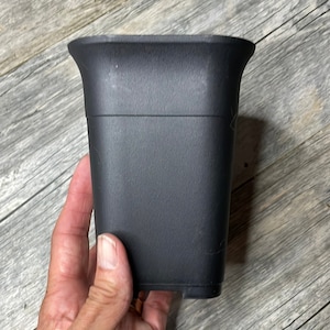 May include: A black plastic plant pot with a rounded top and a square base.