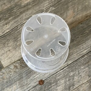 May include: Clear plastic plant saucer with drainage holes. The saucer is 18 cm in diameter and has the text "Made in China" printed on the bottom.