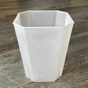 May include: A translucent white plastic planter with an octagonal shape and a tapered design. The container features a wide open top and vertical structural lines along the sides, providing a clear view of the interior space and the base structure.