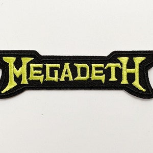 May include: A black embroidered patch featuring the word "MEGADETH" in a bright yellow, stylized font. The patch has a unique shape with pointed ends and a black border. The patch is likely for a jacket or bag.