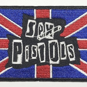 May include: Embroidered patch featuring the Union Jack flag design in red, white, and blue. The words "Sex Pistols" are in white, with a safety pin graphic. The patch has a black border.