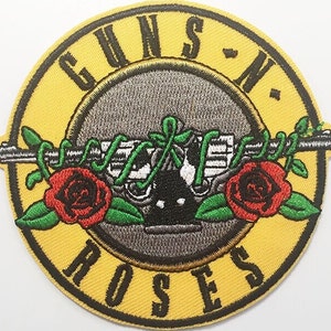 May include: Embroidered patch featuring the Guns N' Roses logo. The design includes a pair of crossed revolvers, roses, and vines, set against a gray background within a yellow circle. The band's name is embroidered in yellow.