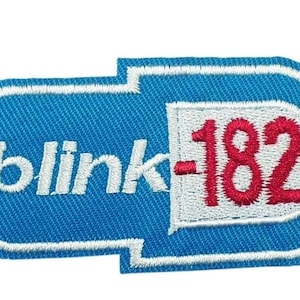 May include: Embroidered patch featuring the band name "blink-182" in white and red on a blue background. The patch has a white border and a pill-shaped design, suitable for clothing or accessories.
