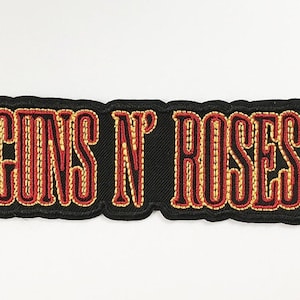 May include: Embroidered patch with the text "GUNS N' ROSES" in red and gold thread on a black background. The patch has a black border and is likely for clothing or accessories.