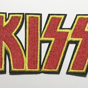 May include: Embroidered patch featuring the word "KISS" in bold, red letters with yellow and black trim. The patch is likely for clothing or accessories, and is a representation of the rock band.
