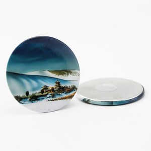 Puede incluir: Un imán redondo de cerámica blanca con una imagen colorida de una escena de montaña nevada con un edificio de estilo pagoda en primer plano. El imán tiene una parte posterior plateada.