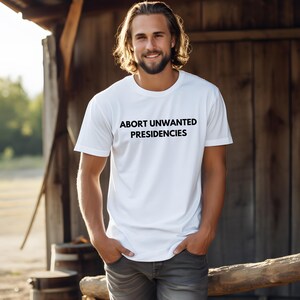 May include: A white t-shirt with the text "ABORT UNWANTED PRESIDENCIES" printed in black on the front.
