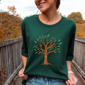 May include: A green t-shirt with a brown tree design. The tree has green leaves with the word "Yellow" written on each leaf. The text "The greatest gift is the love that never fades. Be Just Smith" is written on the trunk of the tree.