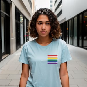 Puede incluir: Una persona con una camiseta azul claro con un parche de bandera arcoíris en el lado izquierdo del pecho.