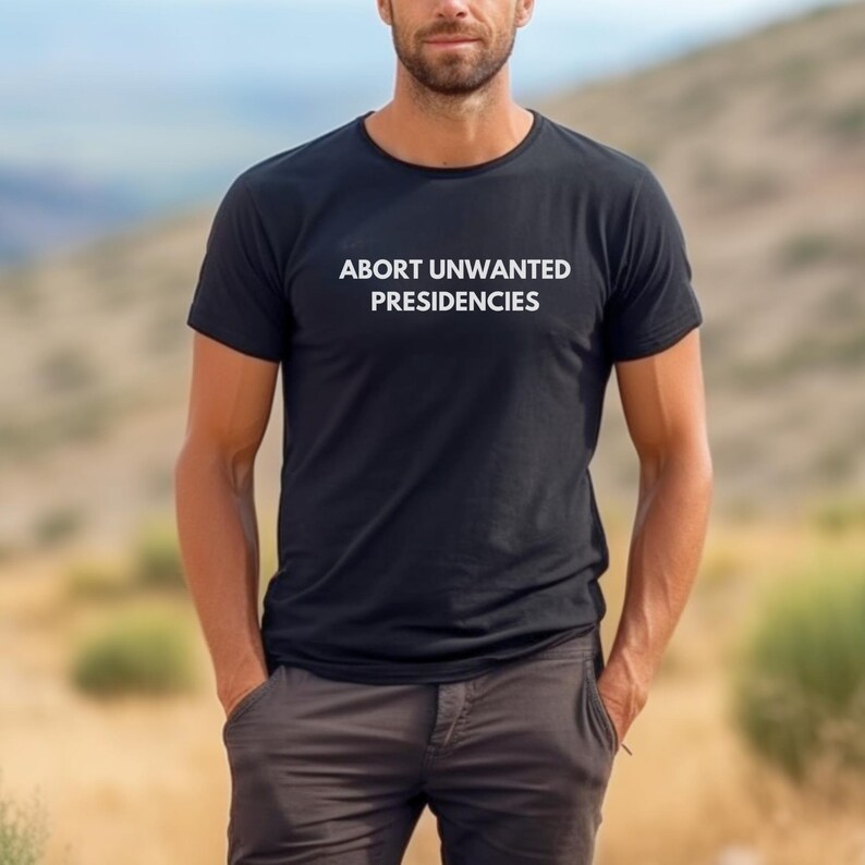 May include: A black t-shirt with the text "ABORT UNWANTED PRESIDENCIES" printed in white on the front.