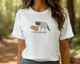 May include: White t-shirt with a cartoon raccoon holding a cookie and the text "Is this gluten free?"