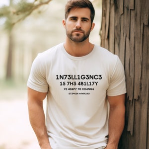 May include: A white t-shirt with black text that reads "1N73LL1G3NC3 15 7H3 4B1L17Y 70 4D4P7 70 CH4NG3 -573PH3SN H4WK1NG"