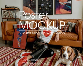 May include: A poster mockup featuring three framed art prints with space-themed designs. A person sits on a rug with a framed poster, and a dog is nearby. The scene includes a brown leather sofa and a shelf with books.