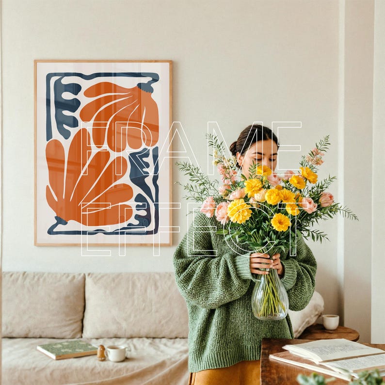 Frame Mockup with Woman in Artistic Minimalist Home – A serene, artistic interior features a woman placing pastel flowers in a vase while a large poster mockup with green edges awaits artwork on the wall behind her. The setting is complete with a soft sofa, book, and coffee cup, highlighted by natural daylight.
