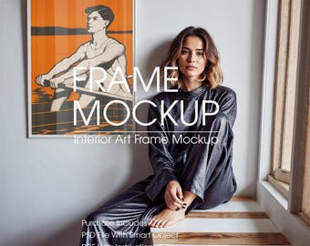 May include: A framed art print mockup featuring a rowing illustration with orange and black tones. The frame is white, and the text "FRAME MOCKUP" and "Interior Art Frame Mockup" are visible. A person is sitting nearby.