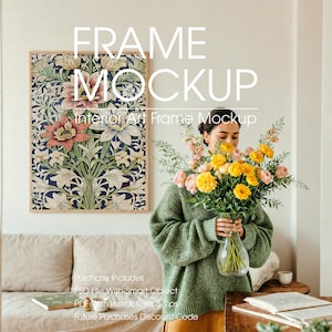 Woman with Poster Frame Mockup in Serene Minimalist Living Room – A young woman with dark hair tied back, wearing an oversized muted green sweater, arranges pastel pink and yellow flowers in a glass vase. Behind her, a large empty wooden poster frame mockup with a soft green border hangs on the wall, ready for artwork. The scene includes a linen-covered sofa, a coffee cup, and an open book on a wooden table, all bathed in soft natural light.