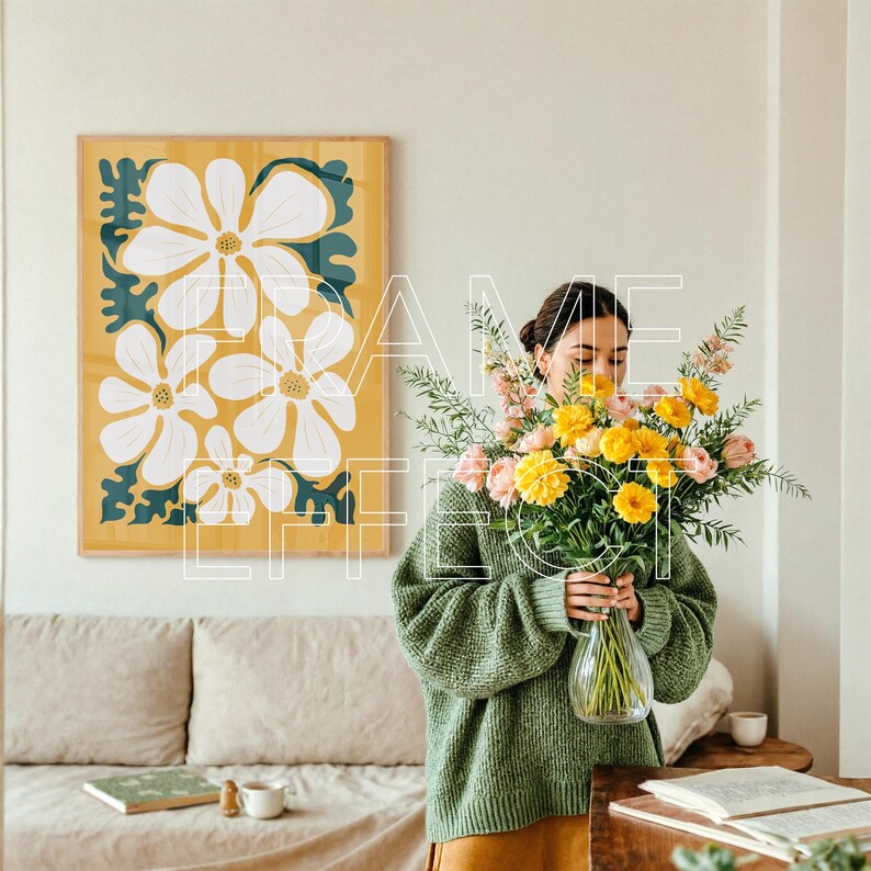 Poster Frame Mockup with Woman and Warm Interior Styling – A young woman stands in a softly lit, modern room with a bouquet of pink and yellow flowers. A wooden poster frame mockup with green trim hangs above a neutral couch, creating an inviting setting that blends relaxed styling with creative energy.