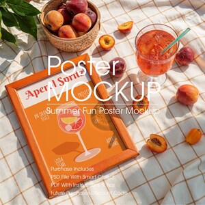 May include: Aperol Spritz poster mockup with a wooden frame, featuring a cocktail illustration. The scene includes a basket of peaches, a glass of the cocktail with a straw, and scattered peach halves on a checkered cloth. The text on the poster reads "Summer Fun Poster Mockup."