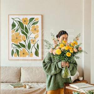 Realistic Art Mockup with Woman in Neutral Living Room – A photorealistic framed art mockup scene shows a woman arranging flowers beside a linen-covered sofa. A large wooden poster mockup with a subtle green frame adds depth to the modern setting, with natural light and a minimal table setup enhancing the calm, curated design.