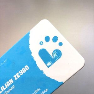 May include: A light blue business card with a white paw print logo and the text "Lilian Zeyad Pet Enthusiast" and "dr.lilian.clinic عيادة ليليان البيطرية".