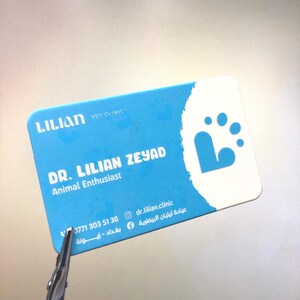 May include: A blue and white business card for a veterinarian named Dr. Lilian Zeyad. The card features a paw print and the text "Lilian Vet Clinic" and "Animal Enthusiast". The phone number 0771 303 51 36 and the social media handles @dr.lilian.clinic and عيادة ليليان البيطرية are also included.