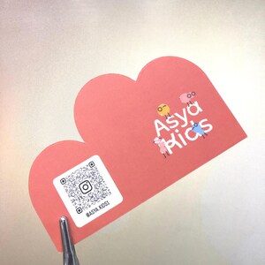 May include: Pink heart-shaped card with a QR code and the text "@ASYA_KIDS1". The card also features a logo with the text "Asya Kids" and a cartoon illustration of three sheep.