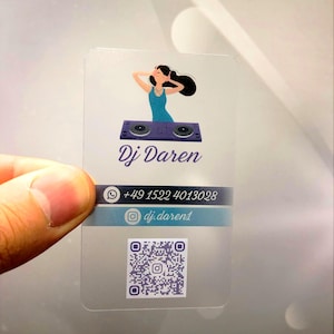 May include: A transparent business card with a cartoon illustration of a woman DJing. The text on the card reads "Dj Daren" and includes a phone number and Instagram handle. A QR code is also included.