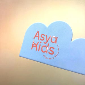 May include: A light blue cloud-shaped tag with the text "Asya Kids" in pink lettering. The text "Live Free Kids" is also written in pink lettering, but it is rotated 90 degrees.