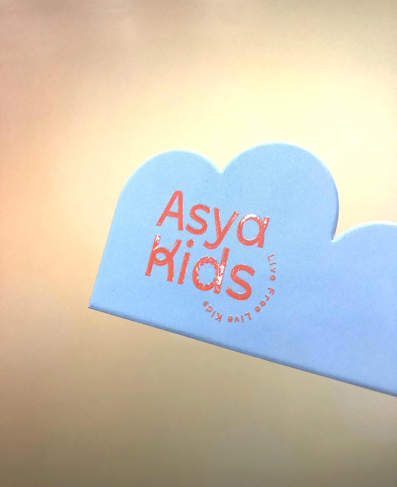 May include: A light blue cloud-shaped tag with the text "Asya Kids" in pink lettering. The text "Live Free Kids" is also written in pink lettering, but it is rotated 90 degrees.