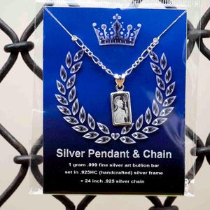 May include: A silver pendant and chain set against a blue backdrop. The rectangular pendant features a figure. The packaging states "Silver Pendant & Chain" and includes details about the silver content and a 61 cm chain.