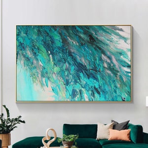 May include: Abstract painting with a teal, blue, and green color scheme. The painting is framed in a gold frame and hangs on a white wall above a green sofa.