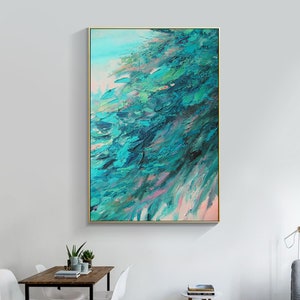 May include: Abstract oil painting with a gold frame. The artwork features textured brushstrokes in shades of teal, turquoise, and green, with hints of pink and a light blue background. The painting is displayed in a modern living room setting.