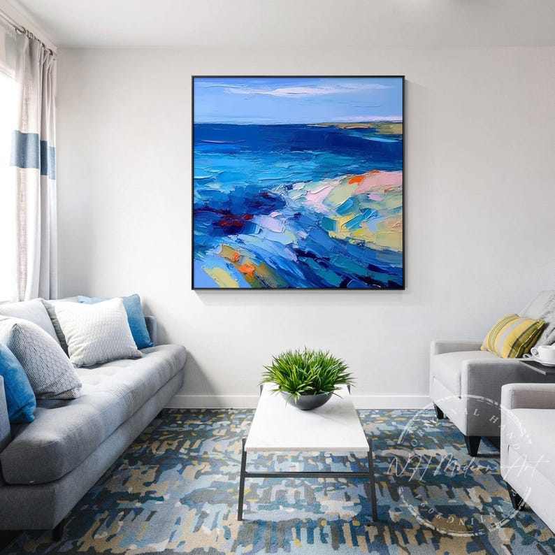 May include: Abstract painting of a seascape with blue, green, and white colors. The painting is framed in black and hangs on a white wall above a gray couch.
