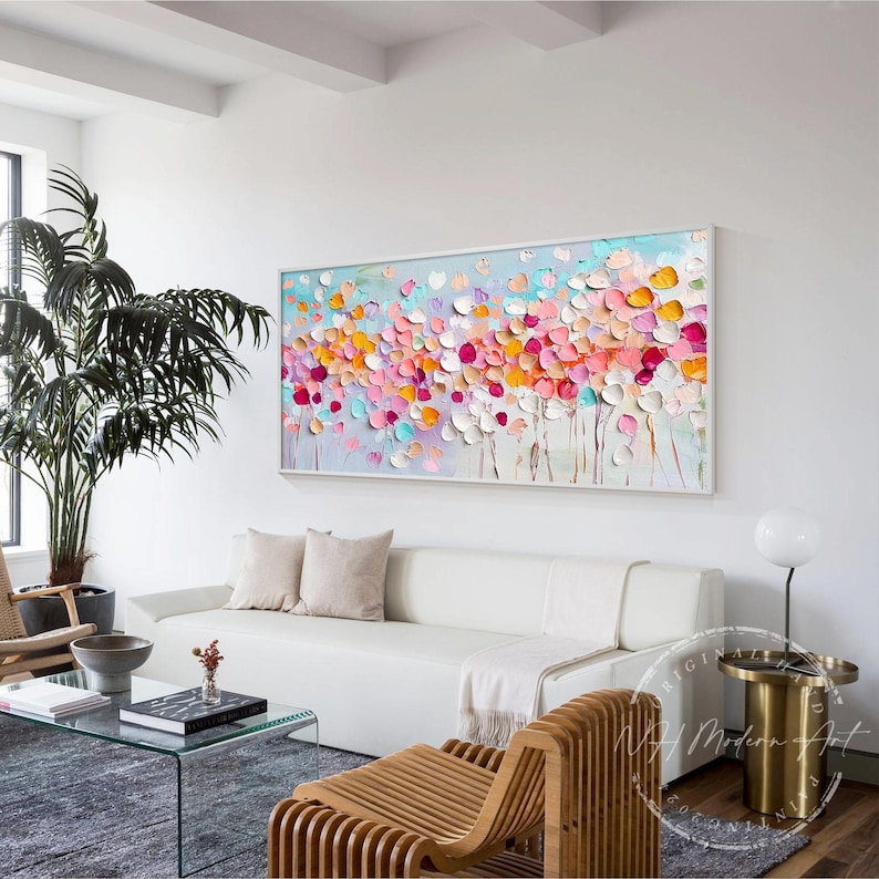 May include: Abstract painting with a colorful floral design. The painting features a variety of pink, orange, yellow, and blue flowers on a light blue background. The painting is framed in a white frame and is hanging on a white wall.